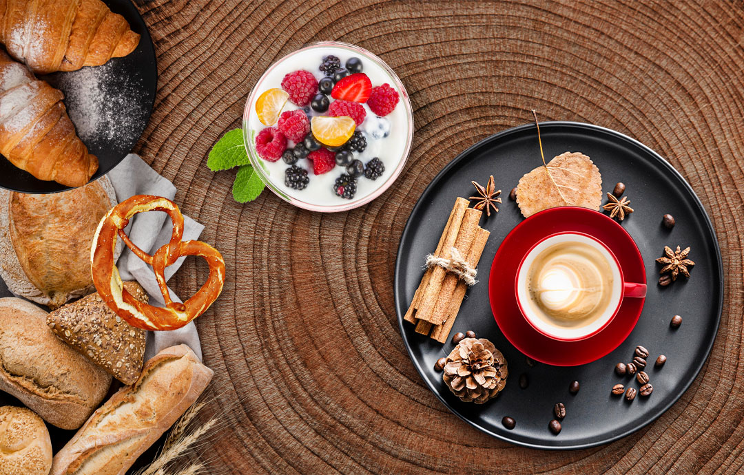 Ofenfrische Croissants, Brezel, Brötchen und ein Cappuccino auf einer Holzplatte in der H&F Bäckerei